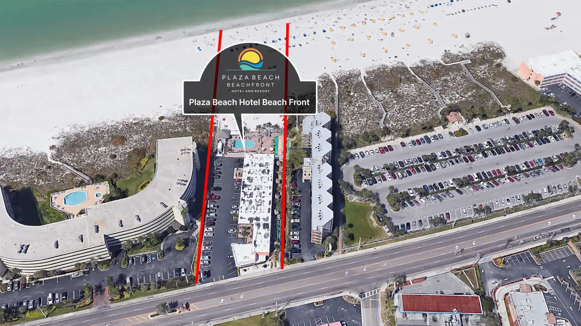 Aerial view of a beachfront hotel with a pool and parking lot.