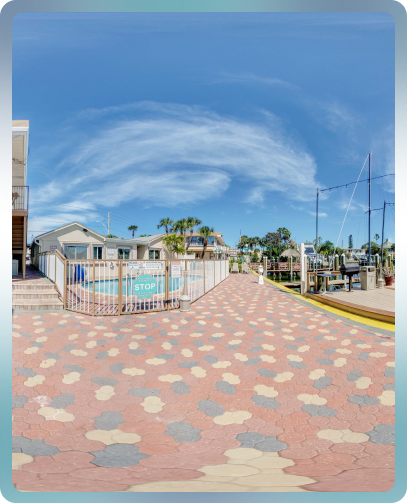 A fenced pool area with a paved path leading to it, surrounded by palm trees under a blue sky.