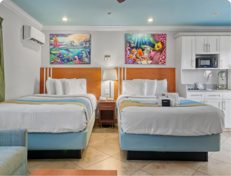 A hotel room with two beds, a kitchenette, and colorful artwork on the walls.